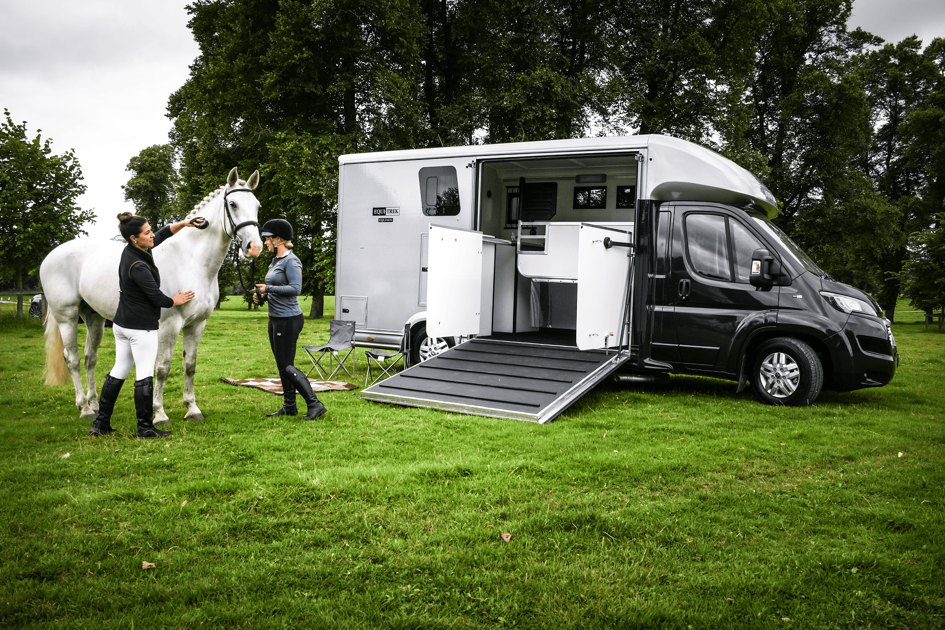 Equi Trek horsebox with rear ramp lowered and two riders standing beside horse in field